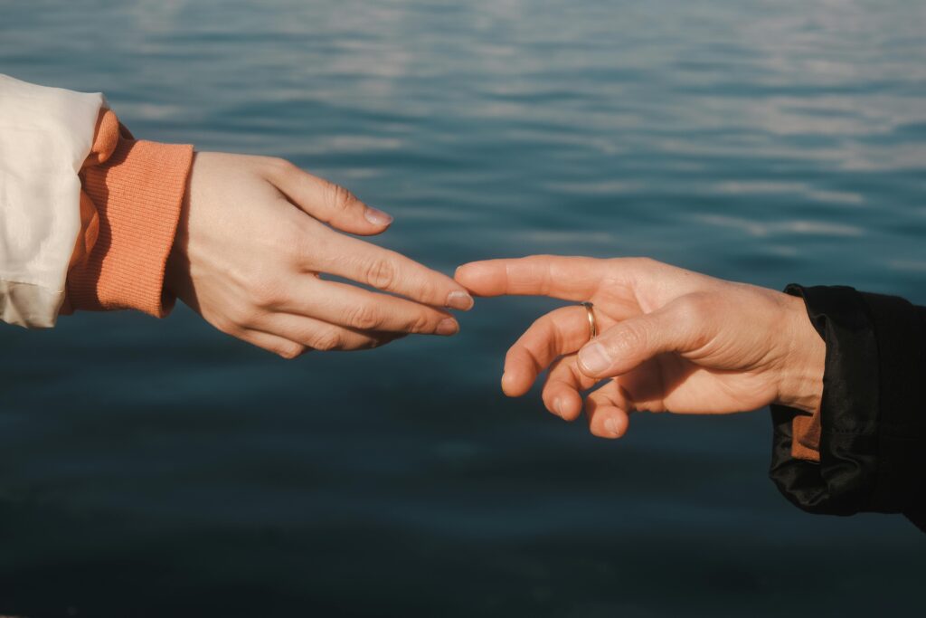 Close-up of two hands reaching across water, symbolizing connection and intimacy.