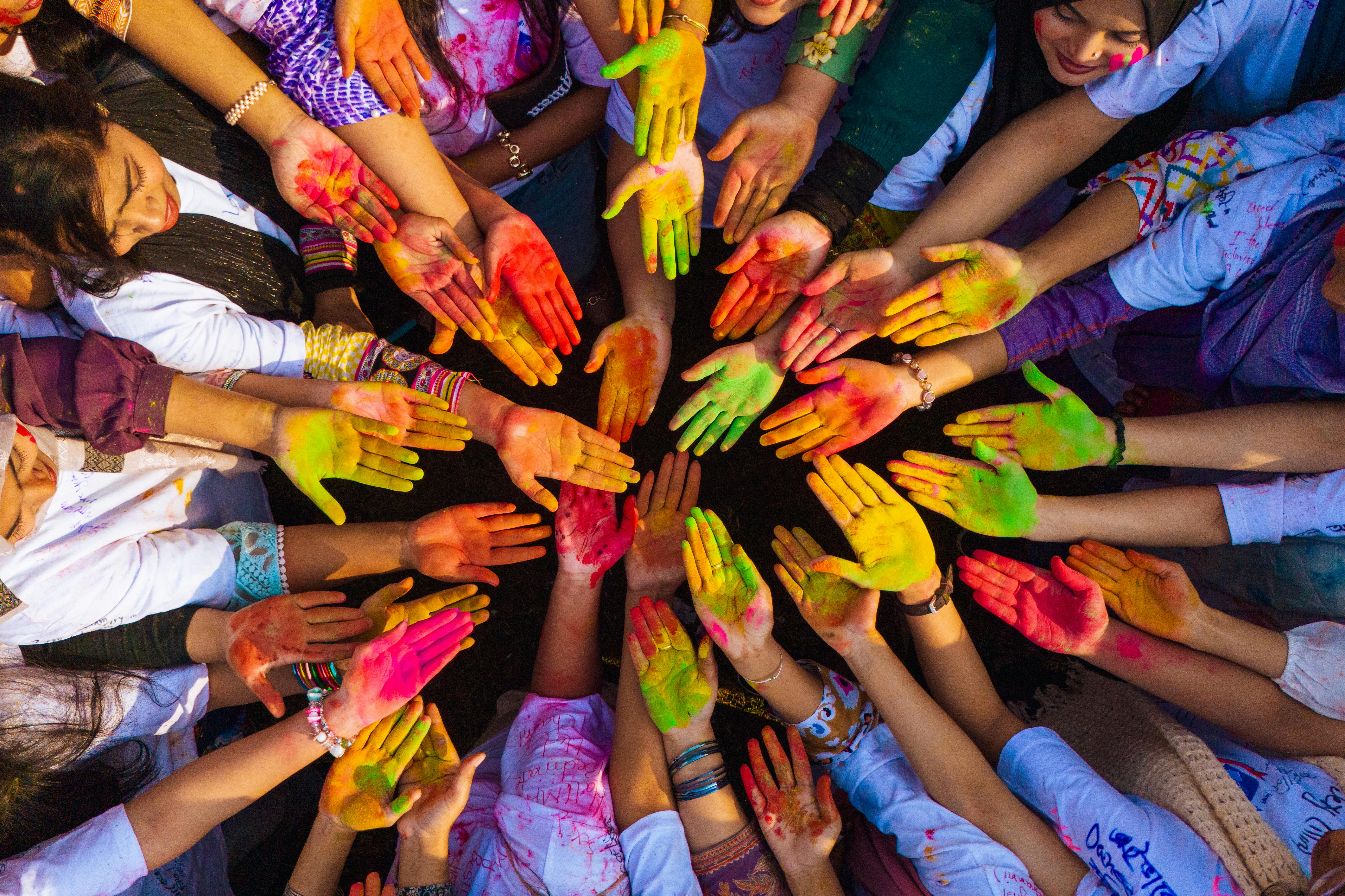 Vibrant top view of diverse hands united in colorful Holi celebration.