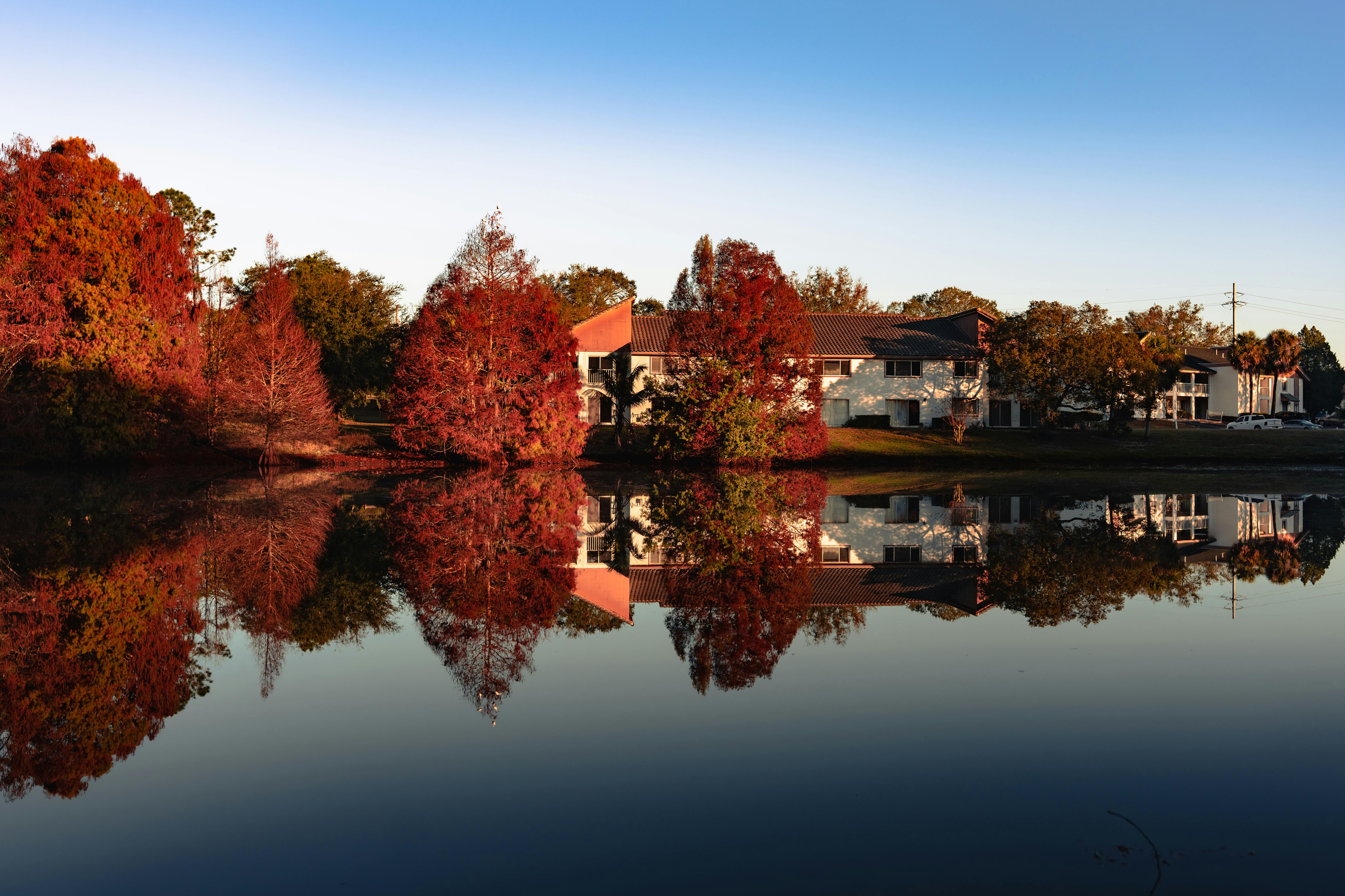 Stunning autumnal scene with reflections of colorful trees and houses on a calm lake. Perfect fall setting.