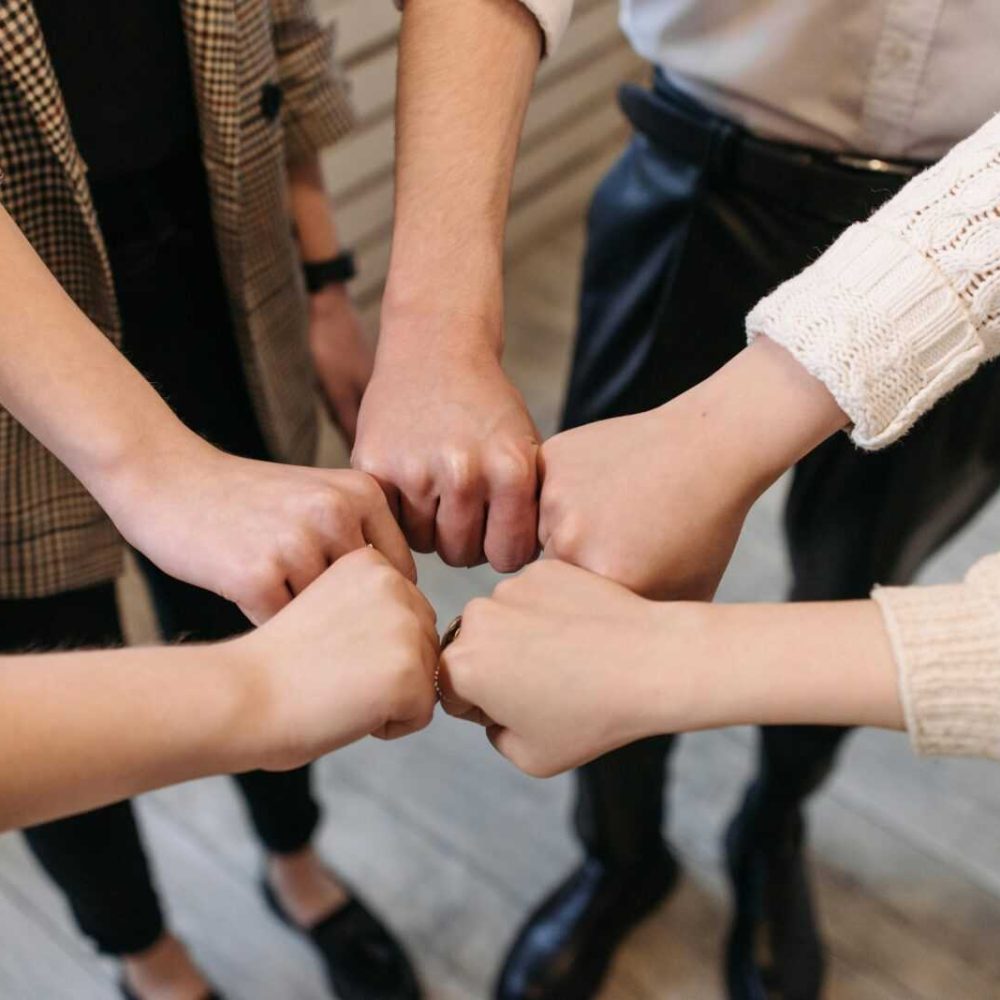 Five people uniting hands indoors, symbolizing teamwork and unity.
